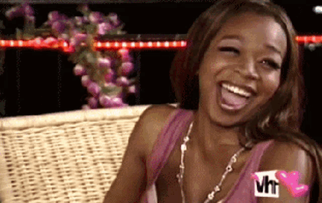 a woman is sitting on a wicker bench and laughing with a vh1 logo on her arm