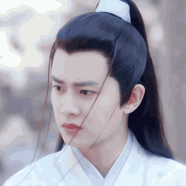 a young man with a ponytail and a white shirt looks to the side