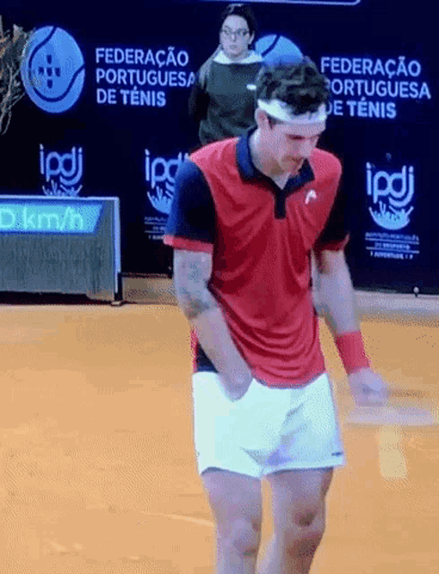 a man in a red shirt and white shorts is playing tennis in front of a sign that says federacao portuguesa de tenis