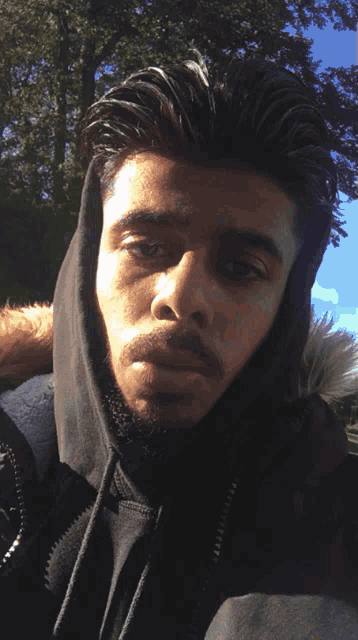 a man in a black jacket with a fur hood looks at the camera
