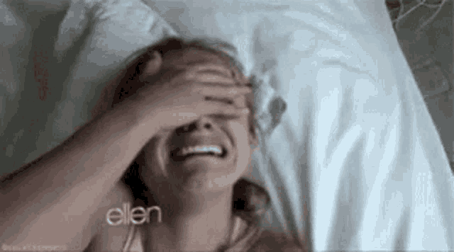 a woman is laying in a bed with her hand on her face .