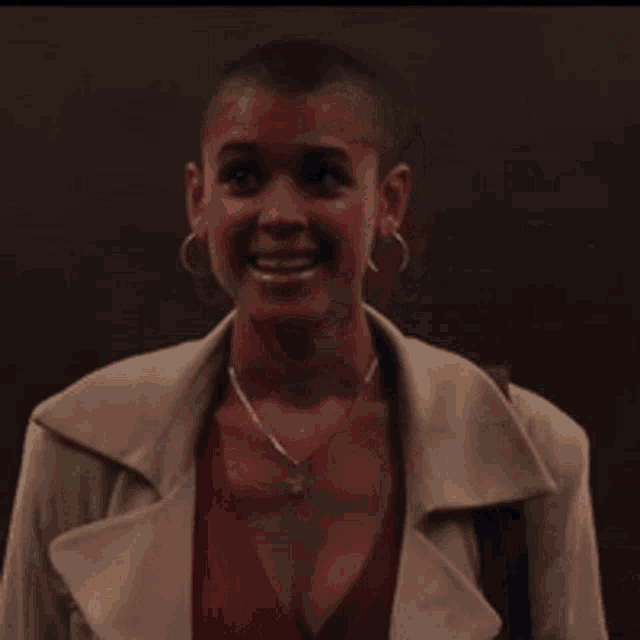 a woman with a shaved head is smiling while wearing a red top and earrings .