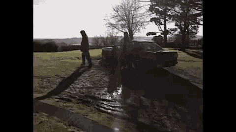 a group of people standing next to a car on a muddy road .