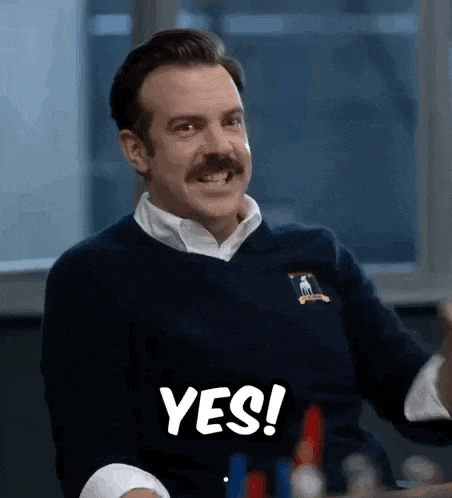 a man with a mustache is sitting at a table and smiling while holding a sign that says yes .