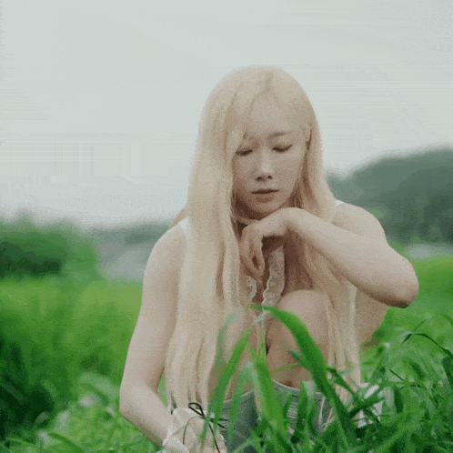 a woman with blonde hair is kneeling in a field