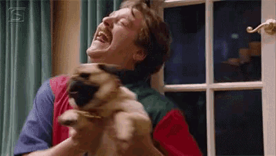 a man is holding a pug dog in his arms while laughing .