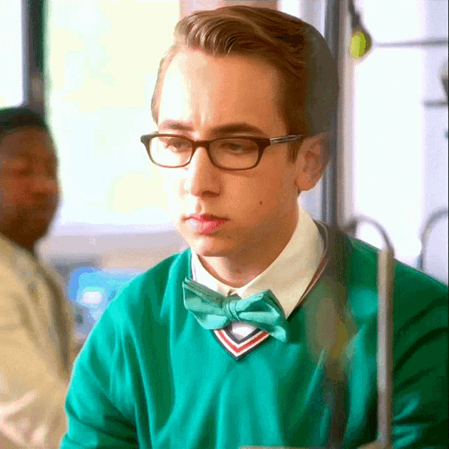 a young man wearing glasses and a green sweater