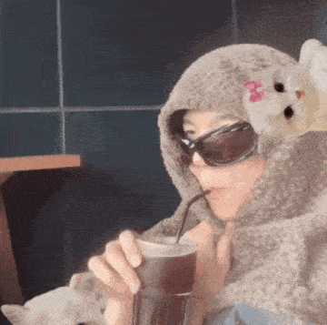 a woman wearing sunglasses and a hooded scarf is drinking from a cup with a straw