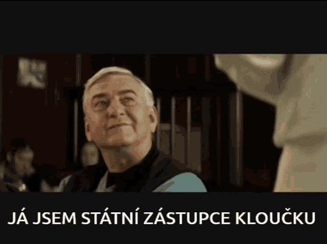 a man in a blue shirt is standing in front of a sign that says ja jsem statni zastupce klouzku