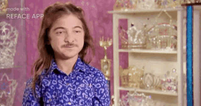 a young man with a mustache is standing in front of a shelf full of crowns .