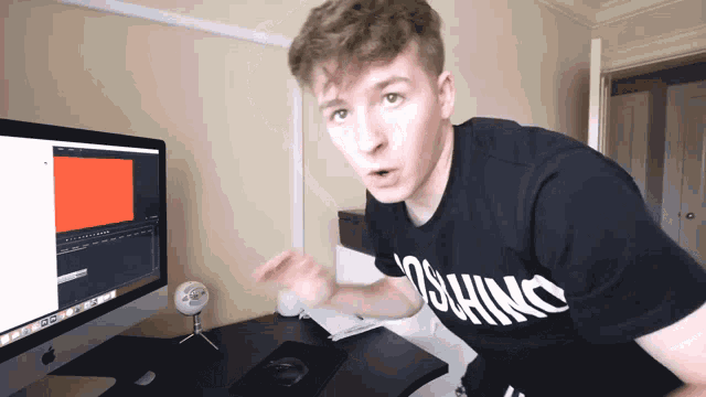 a man wearing a moschino shirt stands in front of a computer screen
