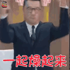 a man in a suit and tie is holding up his arms in the air with chinese writing behind him