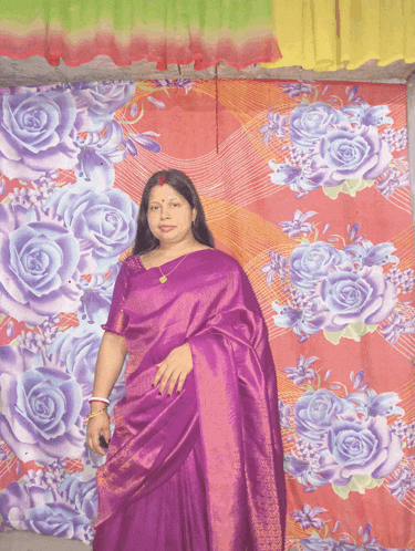 a woman in a purple saree is standing in front of a colorful floral curtain