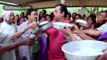a group of people are standing around a man holding a bowl of food .