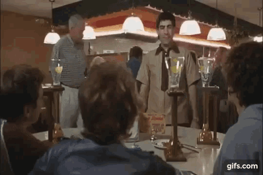 a group of people are sitting at a table in a restaurant and a man is standing in front of them .