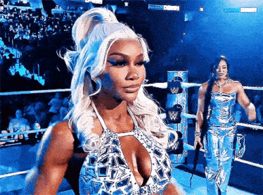 a woman in a blue dress is standing in a wrestling ring with another woman .