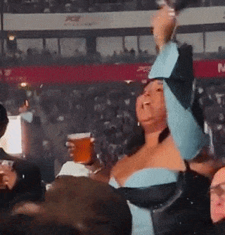 a woman in a blue dress is holding a beer in her hand in a crowded stadium .