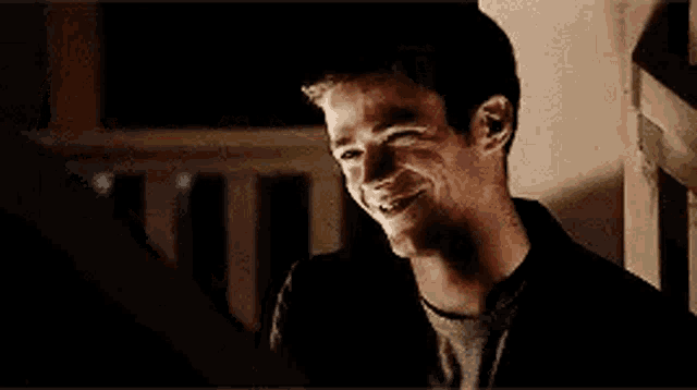a man is smiling while leaning against a wall and looking at the camera .