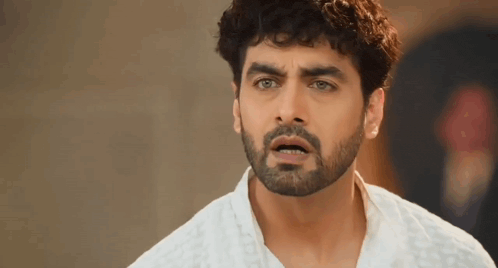 a man with a beard and curly hair is wearing a white shirt and making a surprised face .