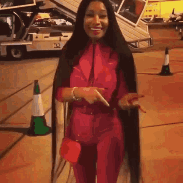 a woman with long black hair is wearing a pink jumpsuit and pointing at something .
