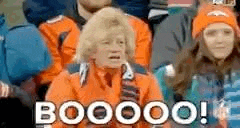 a group of people are sitting in a stadium and one of them is wearing an orange jacket and a hat .