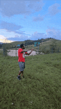 a man wearing a red shirt that says nike on it is standing in a grassy field