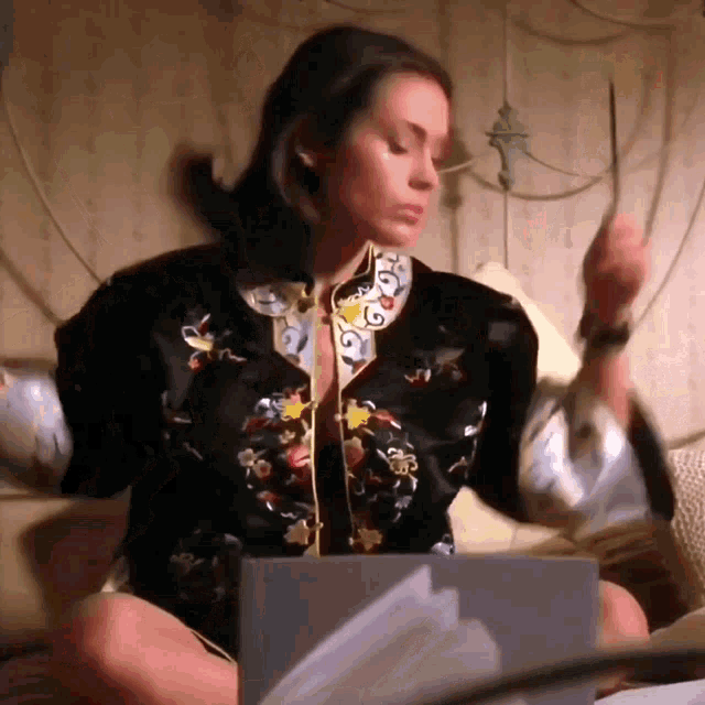 a woman in a black jacket is sitting on a bed with papers in front of her