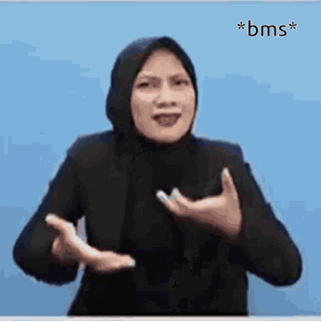 a woman wearing a black hijab is making a gesture with her hands .