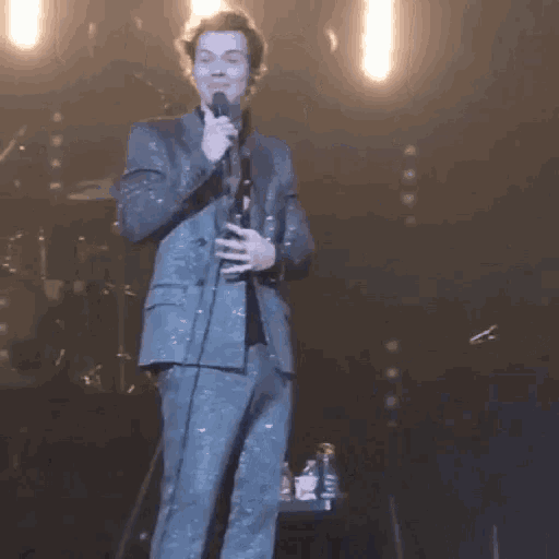 a man in a suit is standing on a stage holding a microphone and singing into it .