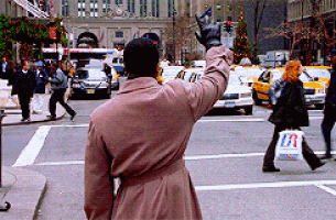 a man in a trench coat is waving at a taxi on a busy street