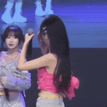 a woman in a pink crop top is holding a microphone while another woman looks on .