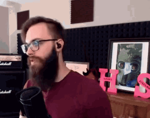 a man with a beard wearing glasses and headphones is singing into a microphone .