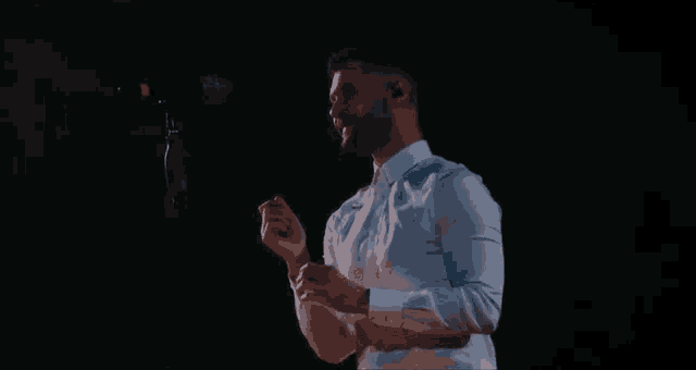 a man in a white shirt is singing into a microphone in a dark room