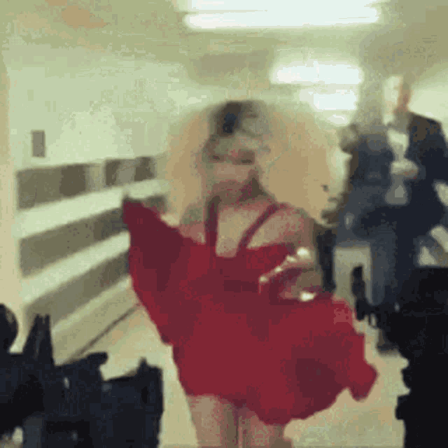 a woman in a red dress is walking down a hallway with a man in a suit behind her .