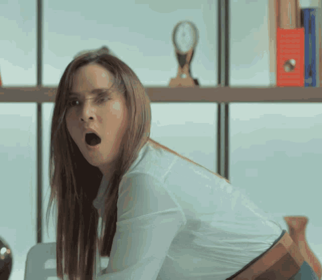 a woman in a white shirt is yawning with her mouth open