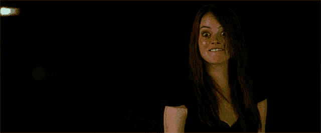 a woman with long red hair is making a funny face in a dark room .