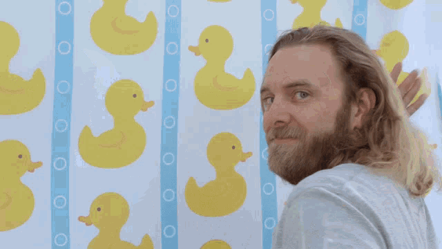 a man with a beard is standing in front of a shower curtain with rubber ducks on it