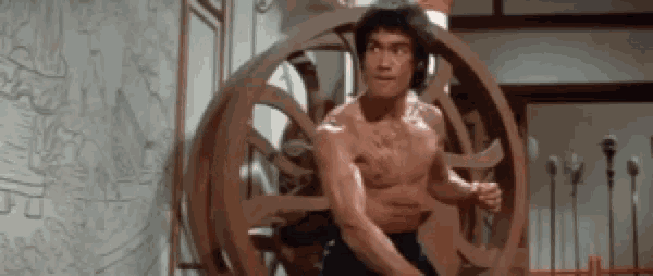 a man without a shirt is standing in front of a wooden circular object .