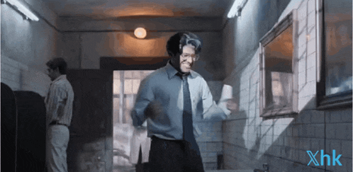 a man in a blue shirt and tie is dancing in a hallway with xhk written on the bottom right