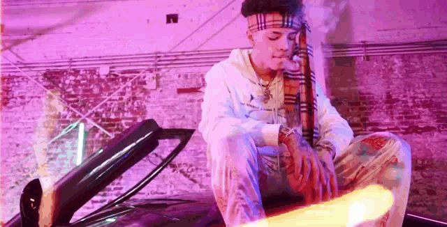 a young man is sitting on the hood of a car in a purple room .