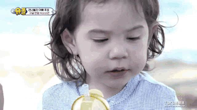 a little girl with long hair is drinking from a yellow bottle with a straw .