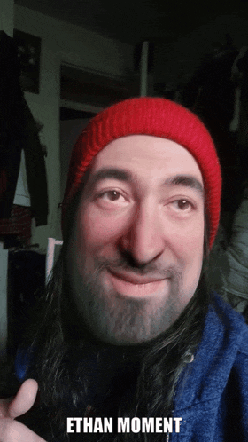 a man with a beard wearing a red hat with the words ethan moment written below him