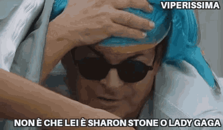 a man wearing sunglasses is holding a blue ice pack on his head
