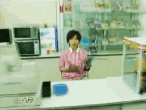a woman in a pink and white striped shirt is behind a counter in a store .