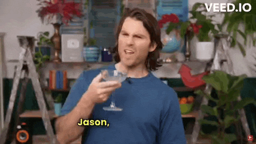 a man in a blue shirt is holding a martini glass and talking to someone .