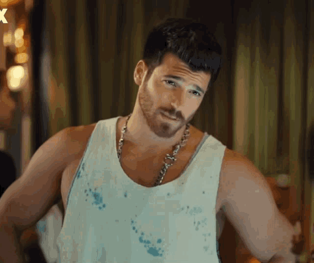 a man with a beard is wearing a white tank top and a chain necklace