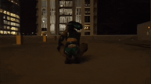 a woman in a green outfit is squatting down in front of a building at night
