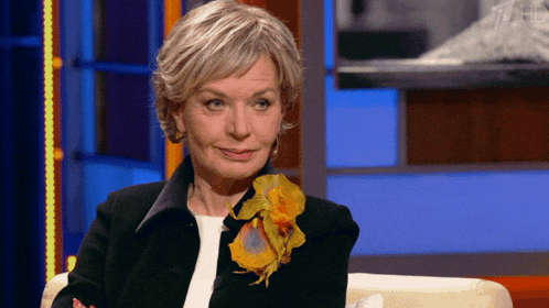 a woman wearing a black jacket and a yellow flower on her collar