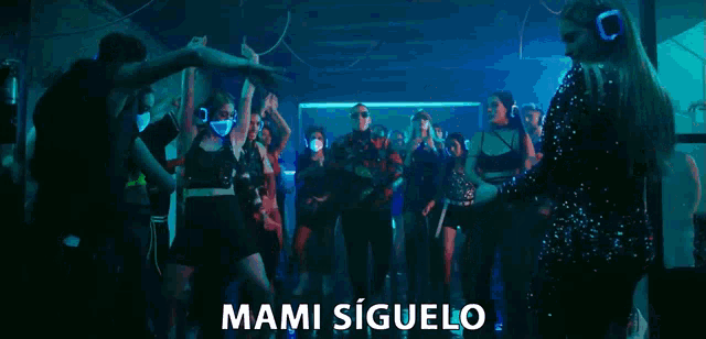 a man wearing sunglasses is singing into a microphone in front of a crowd and the words mami siguelo are visible .