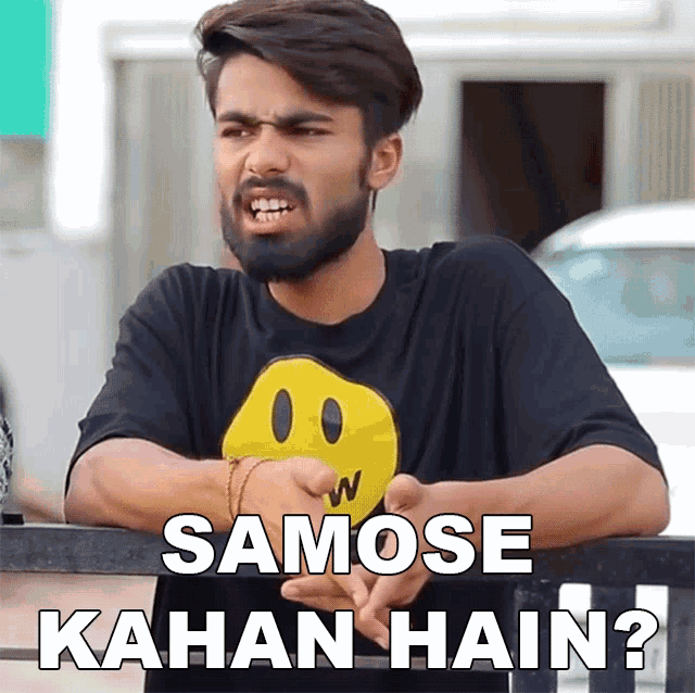 a man with a beard wears a black shirt with a yellow smiley face on it